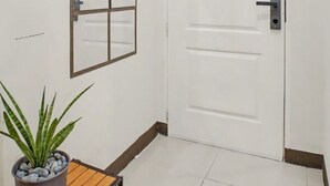 Un couloir avec une porte blanche, un miroir encadré et une plante en pot posée sur une étagère en bois.
