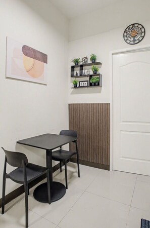 A room with a table and chairs, a clock, shelves with plants, and a door. - Cozy Stay at Winland Tower Residences (Quezon City)