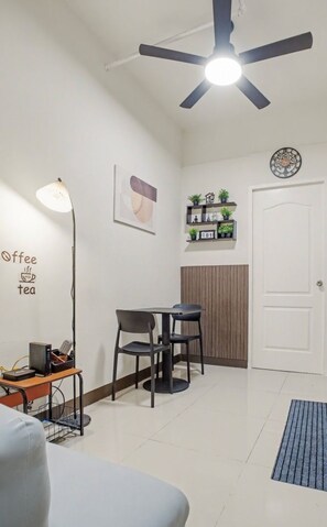 A room with a ceiling fan, a table with chairs, a coffee-themed wall art, a clock, and a door. - Cozy Stay at Winland Tower Residences (Quezon City)