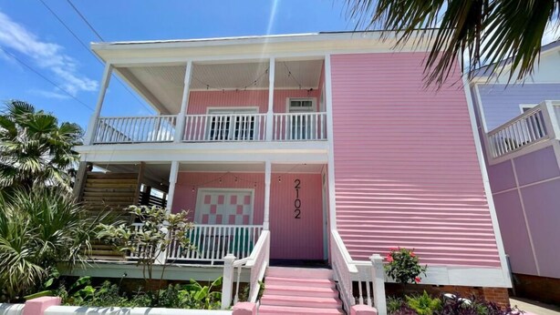 A two-story pink building with a balcony on the upper floor, a front door, and a small porch area. - Pineapple By the Sea (Galveston)