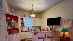 A compact kitchen with a bar area, wooden flooring, and a television mounted on the wall. - Pineapple By the Sea (Galveston)