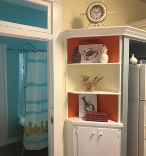 Ein Badezimmer mit Duschvorhang, einer Uhr und einem weißen Schrank mit Regalen.