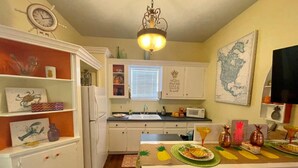 A kitchen with white cabinets, a refrigerator, a microwave, and a dining area with a table set for two. - Pineapple By the Sea (Galveston)