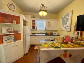 Een keuken met witte kastjes, een koelkast, een magnetron en een eethoek met een tafel gedekt voor twee personen.