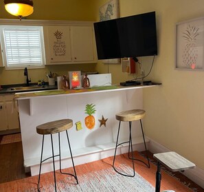 A kitchen with a bar area, a television, and a pineapple-themed wall decoration. - Pineapple By the Sea (Galveston)