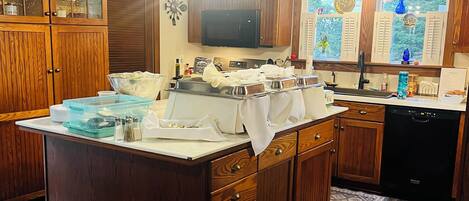 A kitchen with wooden cabinets, a central island, a microwave, and a window with decorative items.