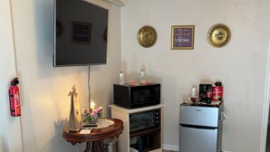 Een compacte woonruimte met een flatscreen-televisie, een magnetron, een kleine oven, een koelkast, een houten tafel met een vaas en een kamerkleed met dessin.
