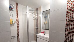 Ein Badezimmer mit Duschkabine aus Glas, einem weißen Waschbecken und einem Spiegel.