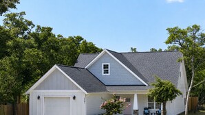 A single-story house with a garage, a covered porch, and a small front yard. - Spacious 4 BDR/3 BA pet friendly <10 min walk to beach + Hot Tub (Oak Island)
