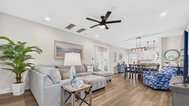 A spacious living room with a grey sofa, a coffee table, and a dining area with a blue chair. - Spacious 4 BDR/3 BA pet friendly <10 min walk to beach + Hot Tub (Oak Island)