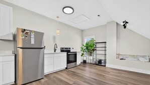 A modern kitchen with a stainless steel refrigerator, white cabinetry, a black oven, and a wooden floor. - Spacious 4 BDR/3 BA pet friendly <10 min walk to beach + Hot Tub (Oak Island)