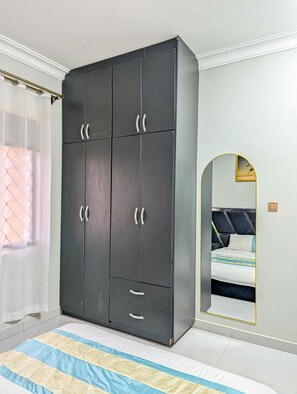 A bedroom with a large wardrobe, a bed with a patterned bedspread, and a mirror on the wall. - Dainty Homes - Kisaasi Kyanja (Kampala)