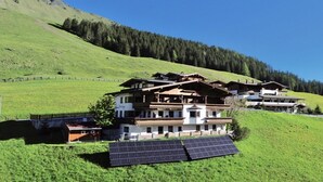 Un immeuble à plusieurs étages, de style architectural traditionnel, entouré d’une colline verdoyante et d’une forêt.