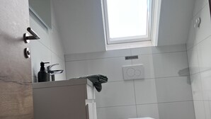 Ein kleines, modernes Badezimmer mit Toilette, Waschbecken und einem Fenster.