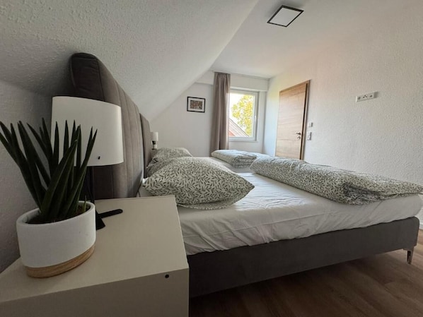 Ein Schlafzimmer mit Bett, Nachttisch, Lampe und einer Zimmerpflanze.