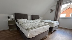 Ein Schlafzimmer mit zwei Betten, einem Nachttisch, einer Lampe und einem Fenster mit Blick auf ein Gebäude.