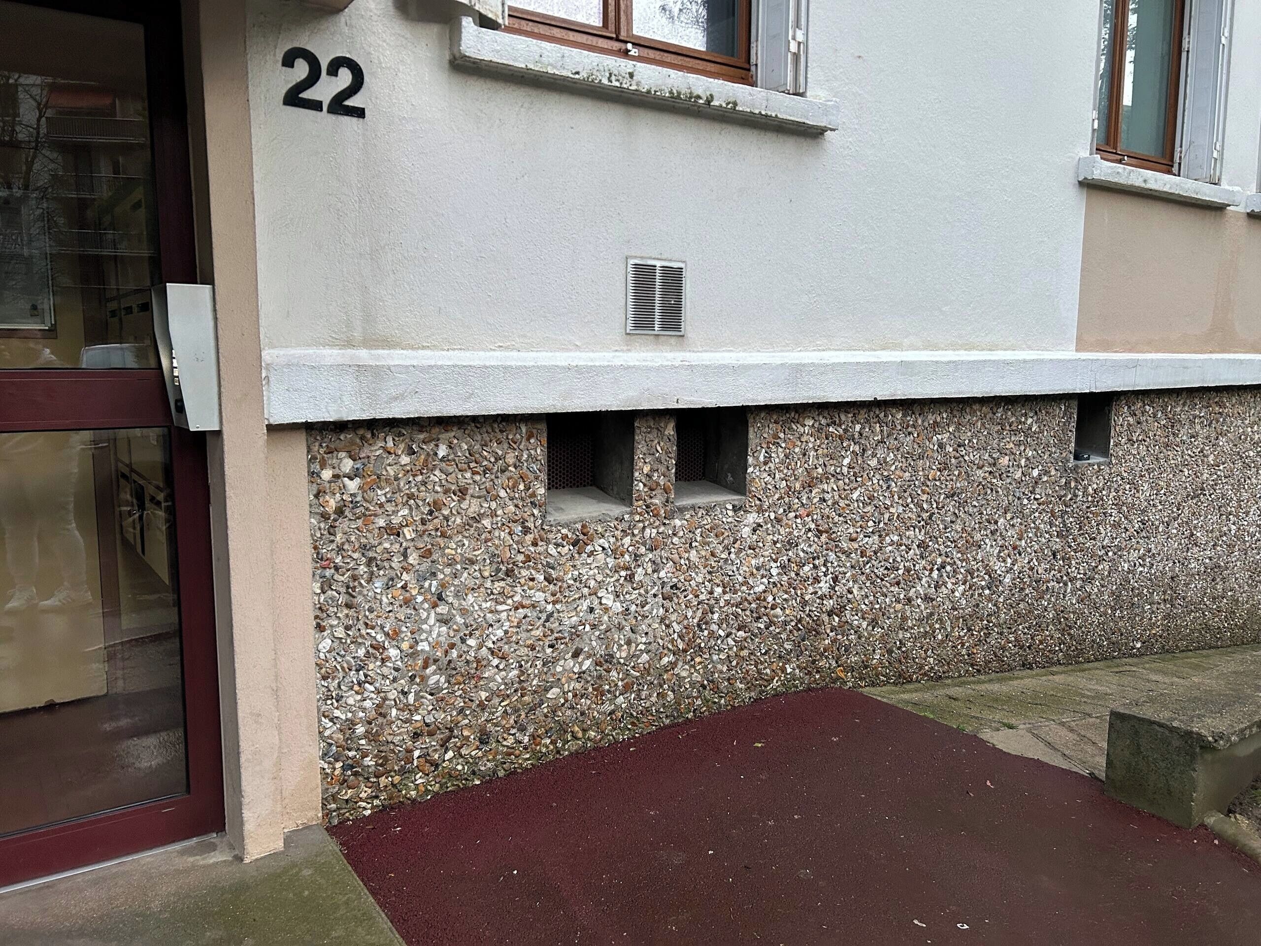 En bygning med en murstensfacade, et skilt med nummer 22, et vindue med ventil og en rød hoveddør i stueetagen.