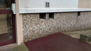 Ein Gebäude mit Steinaußenwand, einem Schild mit der Nummer 22, einem Fenster mit Lüftung und einem roten Eingang im Erdgeschoss.