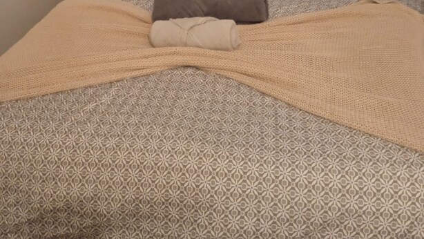 Ein ordentlich gemachtes Bett mit gemusterten Betttextilien, ein gefaltetes Handtuch und ein Fenster mit Vorhängen.