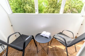 Un balcon avec deux chaises et une petite table, un livre posé sur la table, et une vue sur les arbres par la fenêtre.