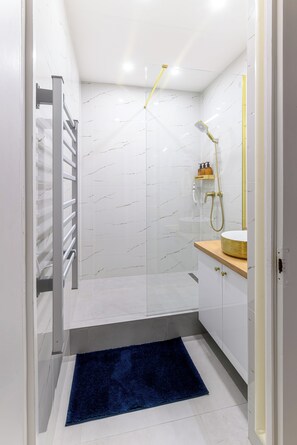 Un baño moderno con cabina de ducha de vidrio, salpicadero de mármol blanco, tocador de madera y alfombra azul.