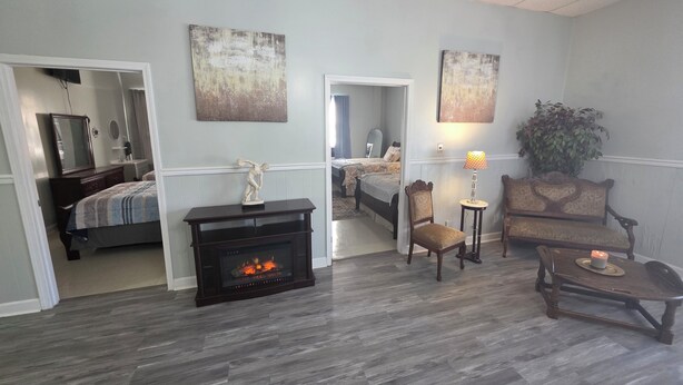 A room with a fireplace, a bed, a chair, a table, and a plant.