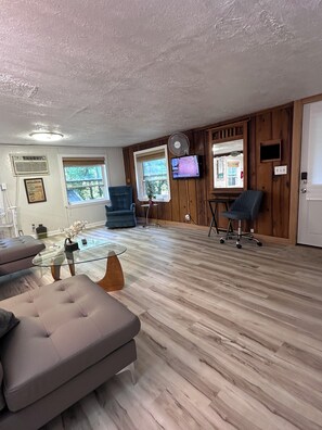A spacious room with a wooden floor, a glass coffee table, a sofa, a TV mounted on the wall, and a window with a view of trees. - White River Cabin - Private
Dock & Wildlife (Gosport)