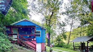 Eine blaue Holzhütte mit einer roten Treppe, umgeben von Bäumen und einem Kiesweg.