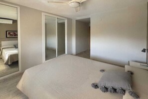 Ein Schlafzimmer mit einem großen Bett, einem Deckenventilator, einer Schiebetür und einem gerahmten Bild an der Wand.