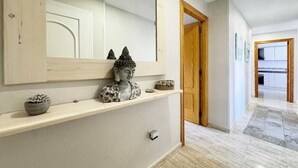Un couloir avec une porte en bois, un miroir et une étagère ornée d’objets décoratifs.