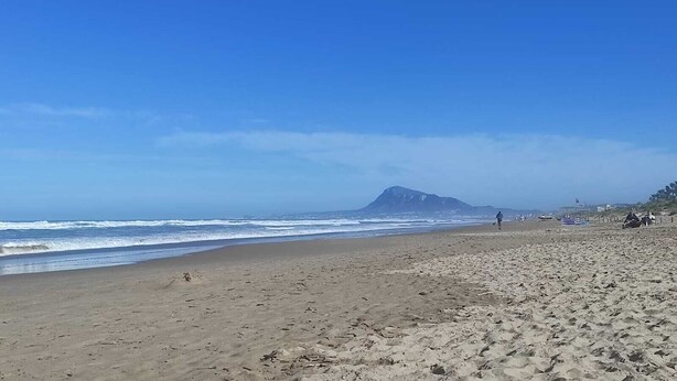 Une plage avec une montagne en arrière-plan, un sol sablonneux et un ciel dégagé.
