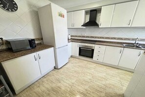 Une cuisine avec des meubles blancs, un four à micro-ondes, un réfrigérateur, une cuisinière et une horloge au mur.