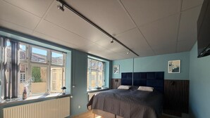 Un dormitorio con cama, ventanas amplias, radiador y luz de techo.
