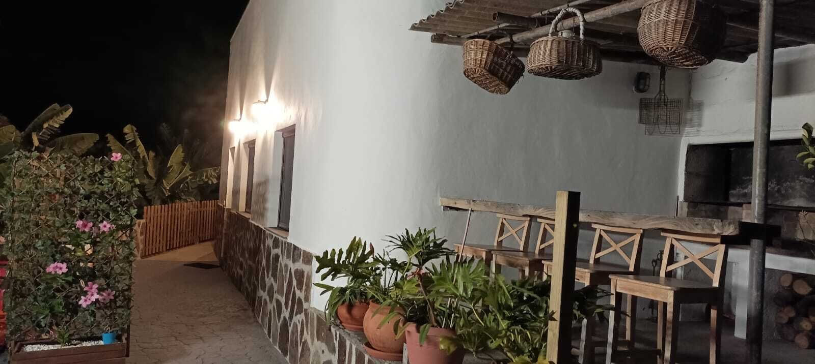 Um edifício branco com parede de pedra, bancos de madeira e plantas em vasos.