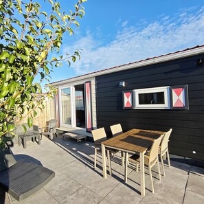 A patio area with a table and chairs, a small bench, and a door leading to a covered space. - Modern 4-person chalet in Zeeland—near the beach, Veere, Middelburg, and Domburg (Serooskerke)