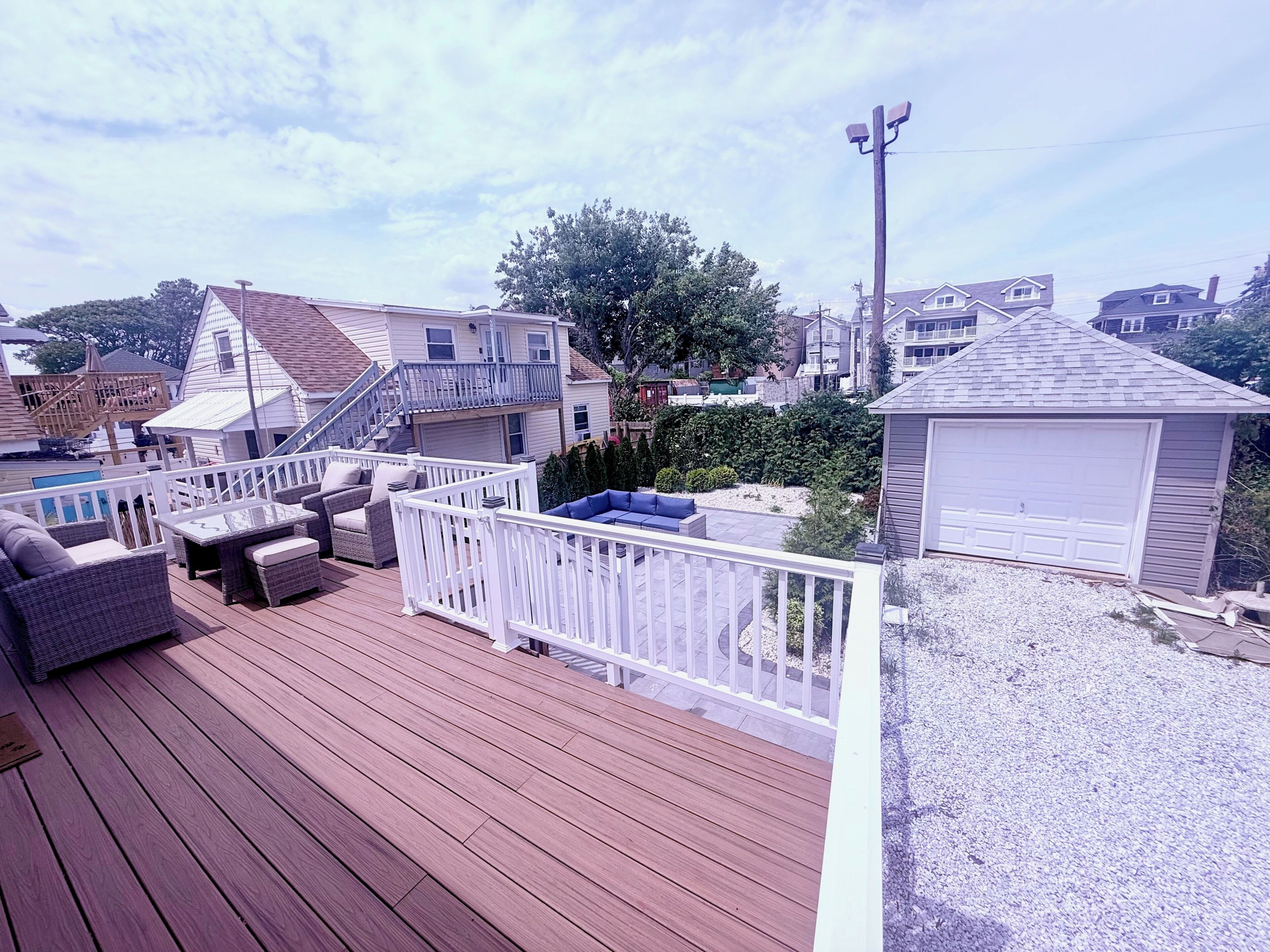Um deck de madeira com móveis de exterior, uma cerca branca e uma garagem.