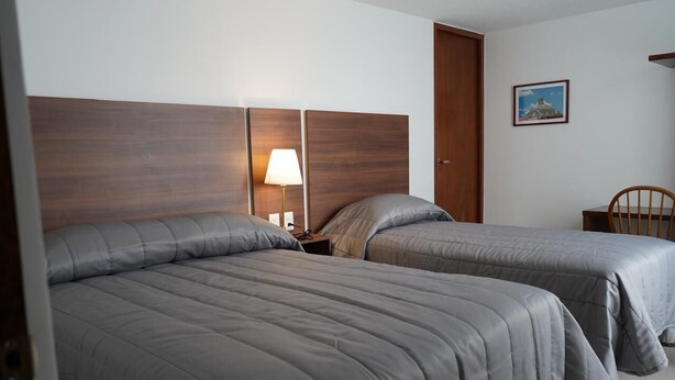 Habitación de hotel con dos camas, cabecera de madera, mesita de noche con lámpara y un cuadro en la pared.