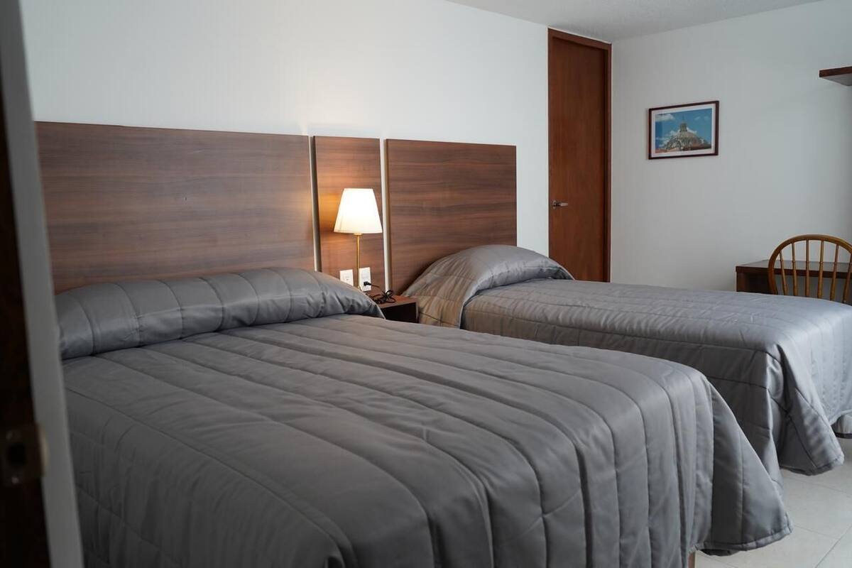 A hotel room with two beds, a wooden headboard, a nightstand with a lamp, and a framed picture on the wall.