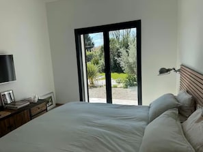 A bedroom with a bed, a TV, a bedside table, and a view of a garden through a sliding door. - Magnificent Villa With Swimming Pool in Marseille (Marseille)