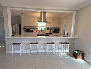 A kitchen with a central island, white bar stools, and a large window.