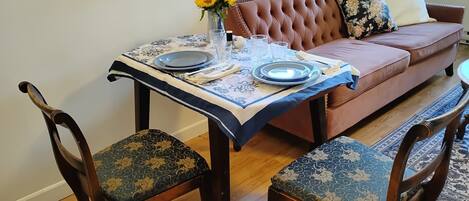 Un comedor con una mesa preparada para dos personas, un sofá y un jarrón con flores.