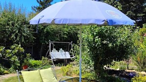A patio area with a metal table and chairs, a swing set, and a blue umbrella. - Victoria Garden Suite (Victoria)
