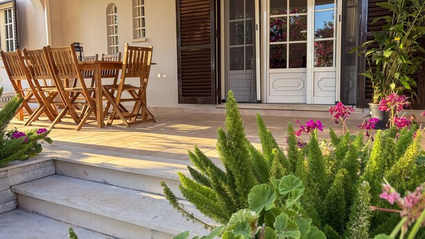 Eine Terrasse mit Tisch und Stühlen, einige Stufen zu einer Tür sowie verschiedene Pflanzen.