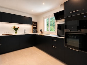 A modern kitchen with black cabinetry, a coffee machine, and a window with a view of greenery. - FAMILY VILLA 190 m² (190 sq.m.) - UP TO 14 PEOPLE - GARDEN 2 500 m² - BEACHES 5 min away (Vendays-Montalivet)