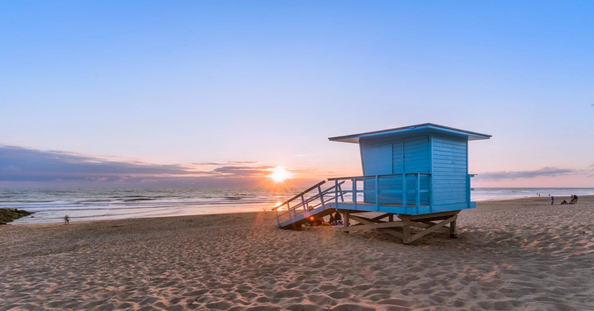 A lifeguard tower on a beach with a clear sky and the sun setting in the background.