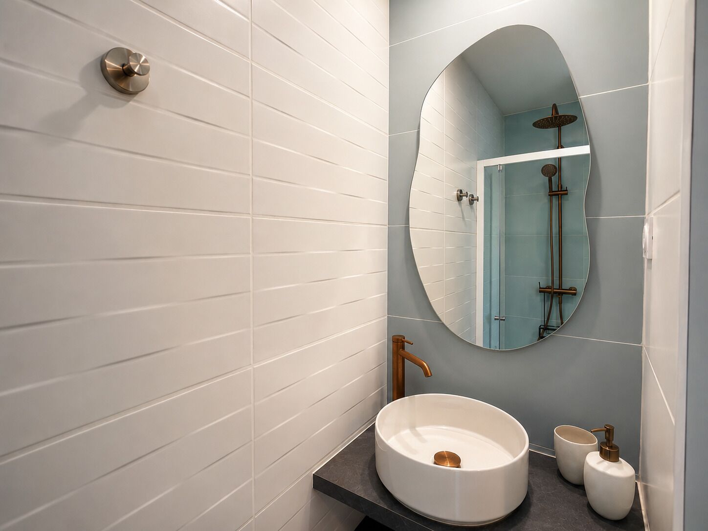 Une salle de bain avec des murs recouverts de carreaux blancs, un miroir rond, un lavabo et une douche.