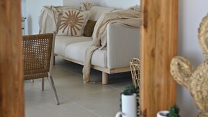 Quarto com sofá, uma poltrona de vime, espelho e objetos decorativos, incluindo um painel de parede tecido e uma planta.