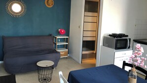 Una habitación con cama, una mesita, un estante con una flor, un microondas y un armario.