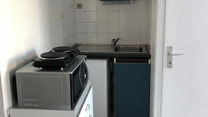 Cocina compacta con microondas, un refrigerador pequeño, un lavamanos y un armario azul.