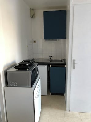 A compact kitchen with a microwave, a small refrigerator, a sink, and a blue cabinet.